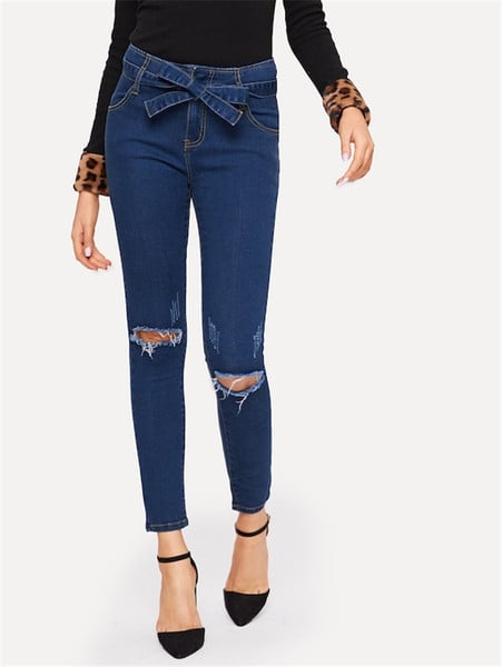 Modern női hosszú farmer szakadt motívumokkal és kék övvel