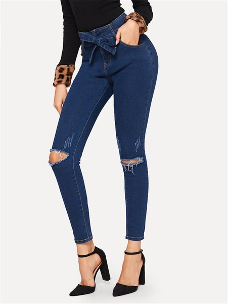 Modern női hosszú farmer szakadt motívumokkal és kék övvel